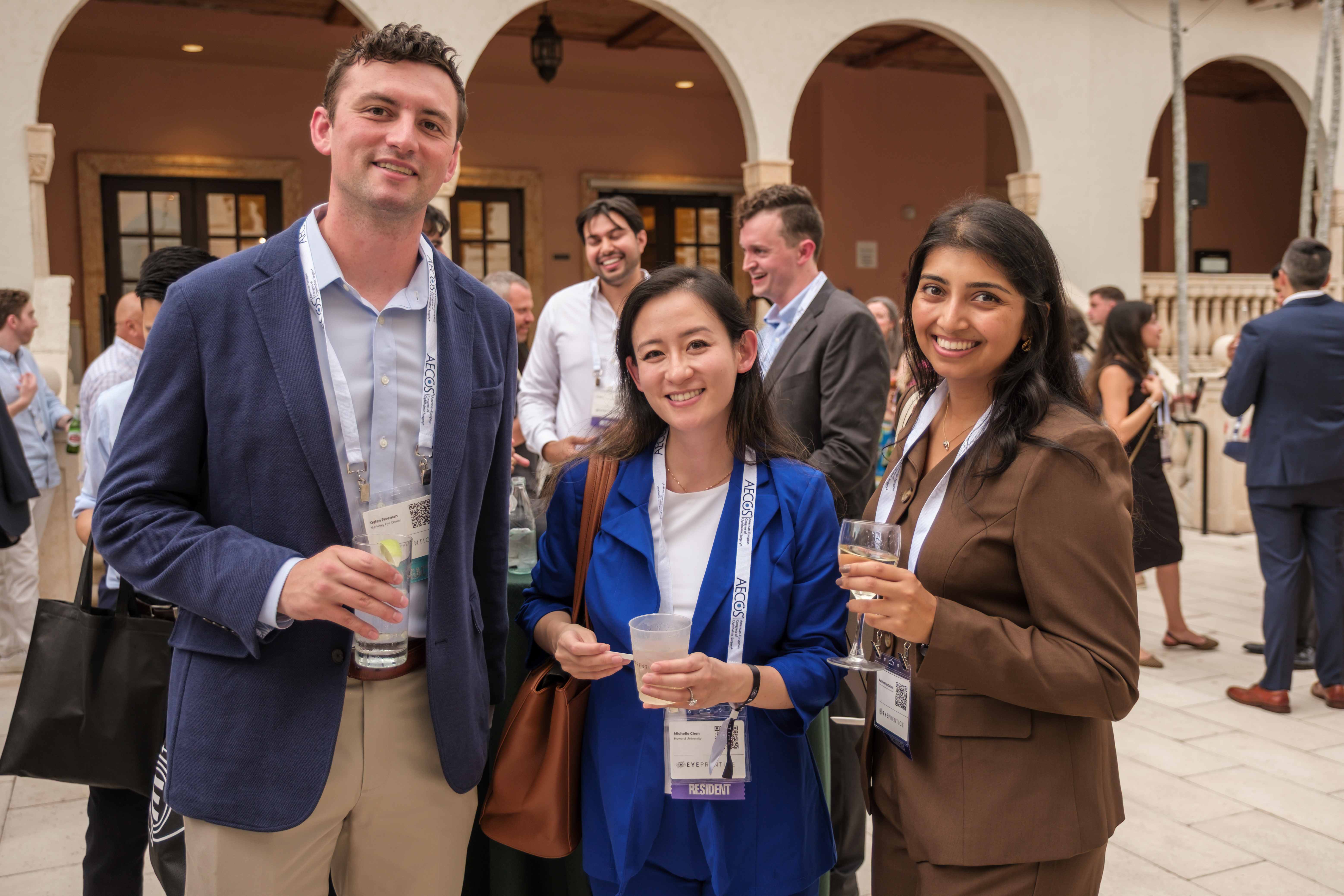 Three residents posing with drinks at a courtyard reception